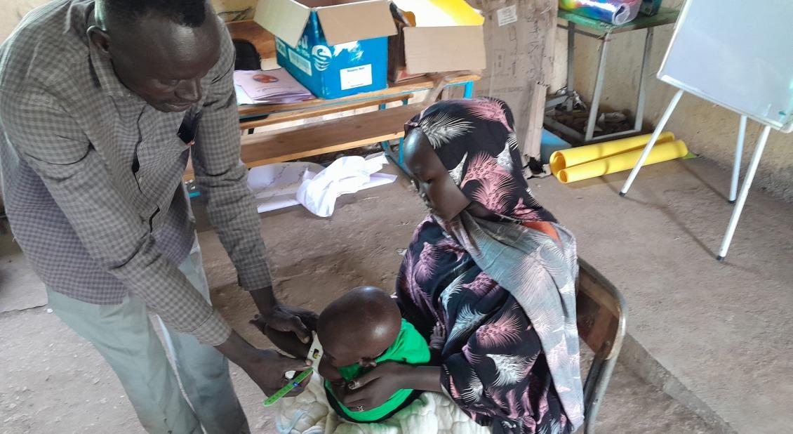 A woman in Sudan holds her baby as he is screened for malnutrition with a mid-upper arm circumference (MUAC) band. /Photo by Pedro Javaloyes